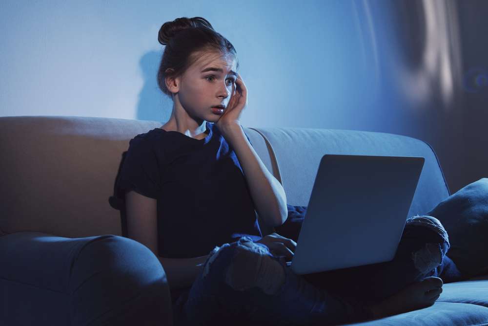 Przestraszona dziewczynka patrzy w ekran laptopa