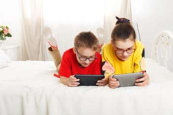 Rodzeństwo leży na łóżku z tabletami w dłoniach