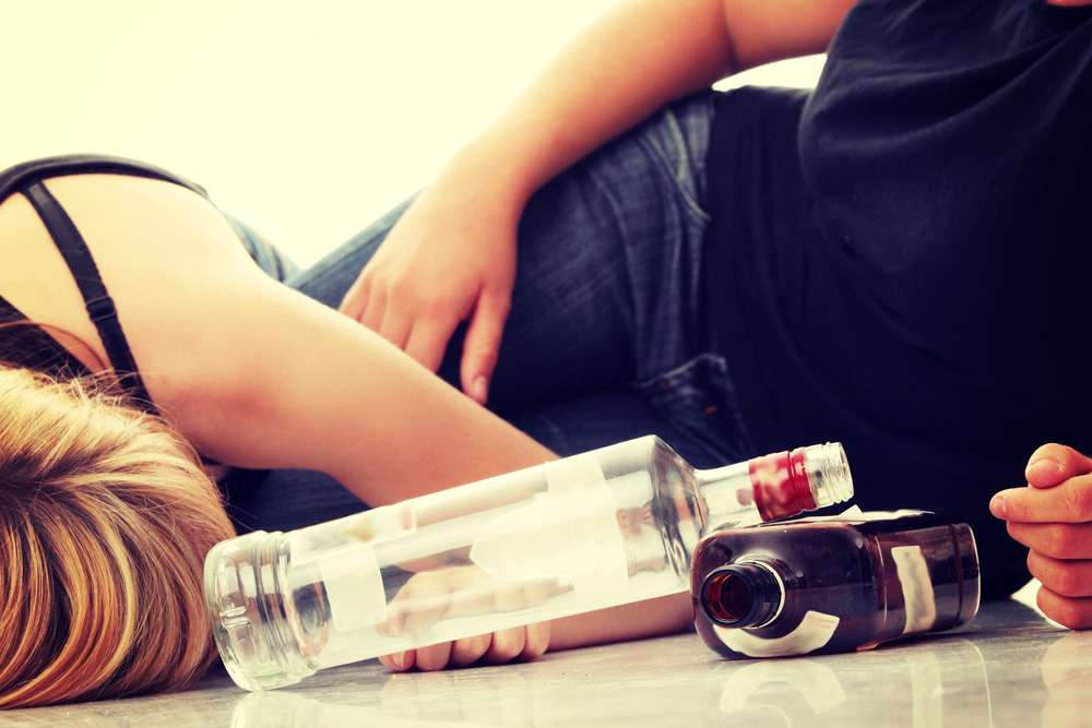 Kobieta i mężczyzna leżą na podłodze obok butelek alkoholu