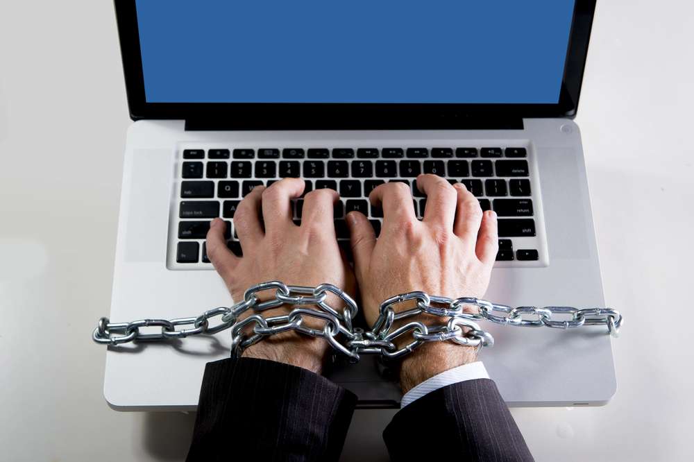 Ręce mężczyzny spięte łańcuchem na klawiaturze laptopa