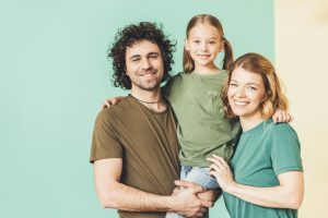 Młodzi rodzice z kilkuletnią córką, szczęśliwa rodzina na zielonym tle